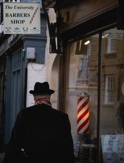 白天，一名身穿黑色西装夹克、戴黑色帽子的男子站在商店附近